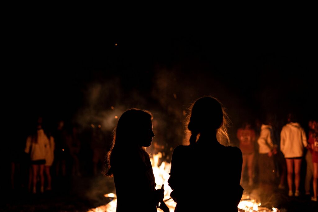 A gathering around a bonfire with silhouetted figures creating a warm night scene.